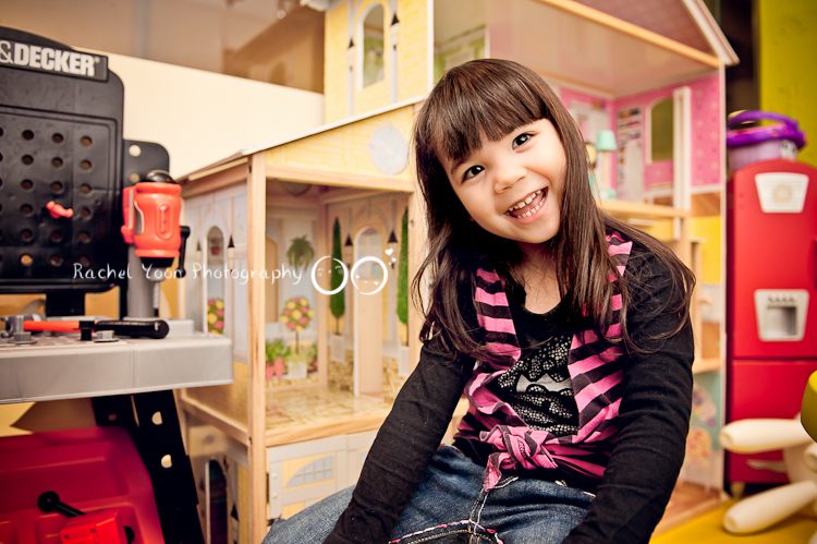 a smiling girl in front of a toy house
