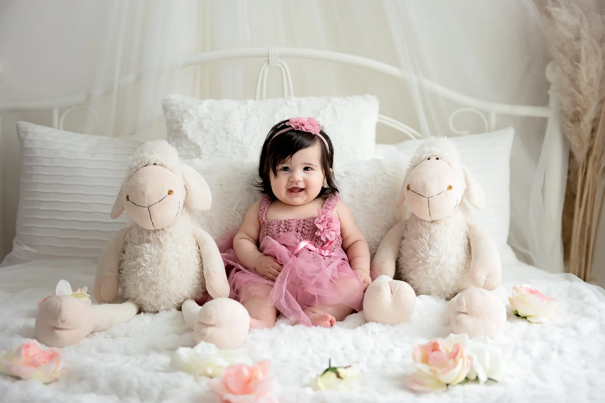 100 days old girl sitting with stuffy lamb on the bed